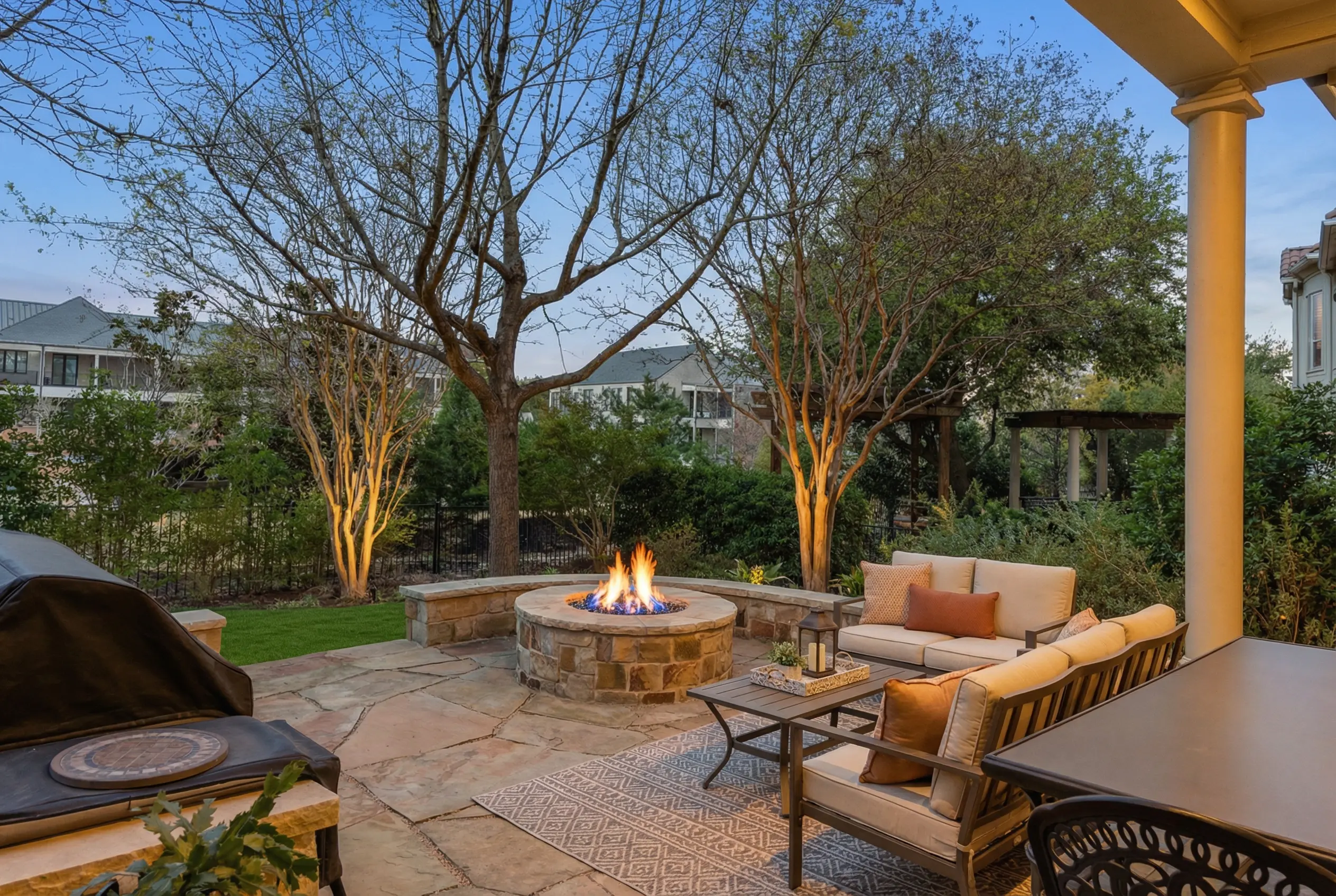 Resort-style backyard with stone fire pit, outdoor lounge, and covered porch at twilight
